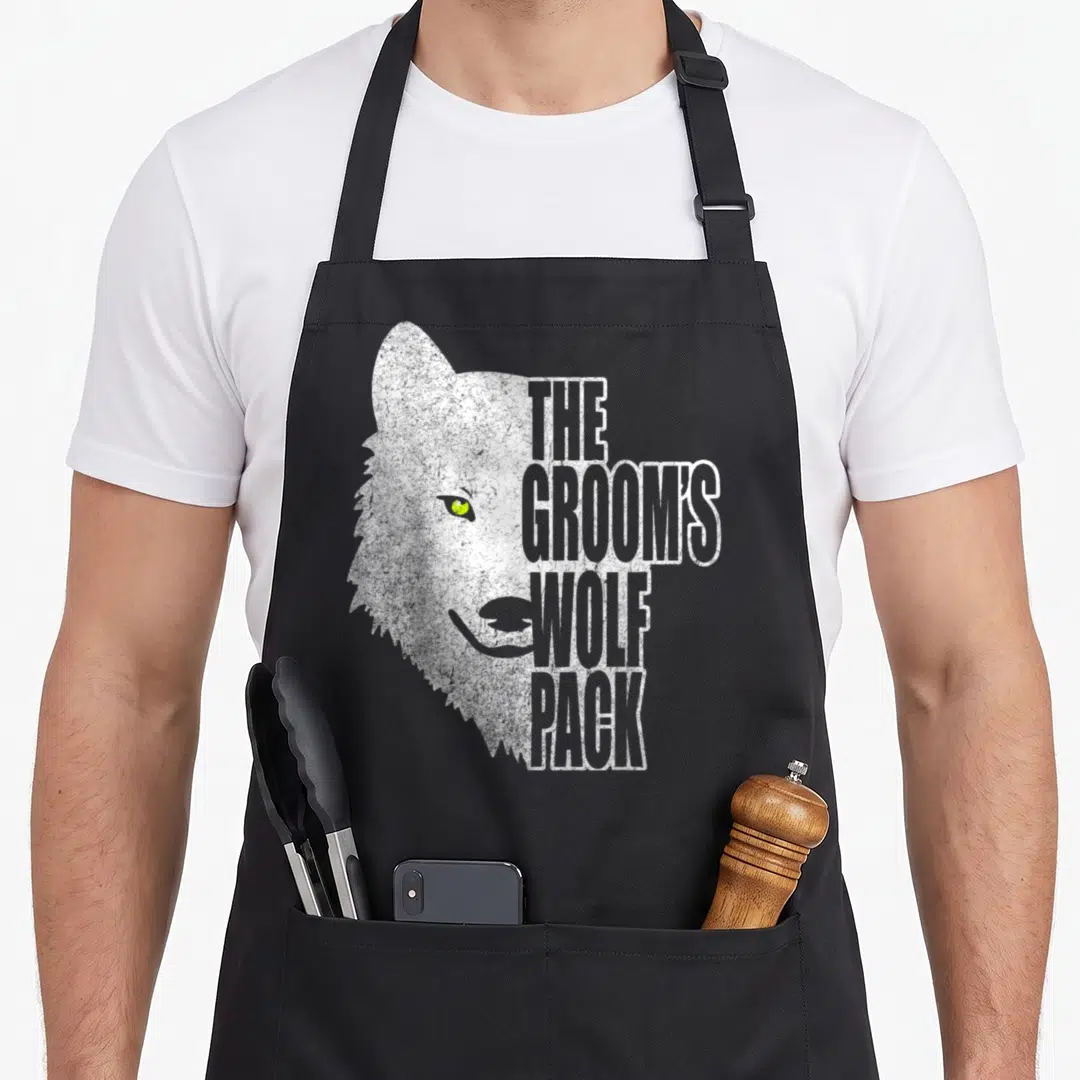Groom police squad apron - Distressed wolf head with yellow eye and stacked text reading The Groom's Wolf Pack — shown on a black cotton canvas apron against a white background