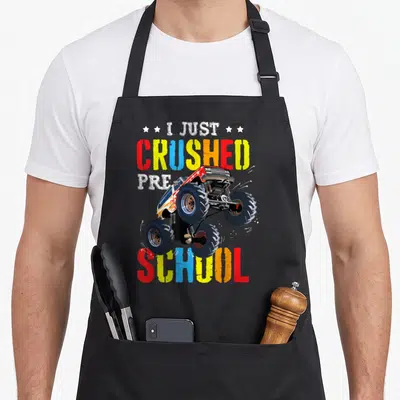 Preschool truck aprons - I Just Crushed Pre School monster truck cartoon with four stars and multicolored text — shown on a black cotton canvas apron against a white background