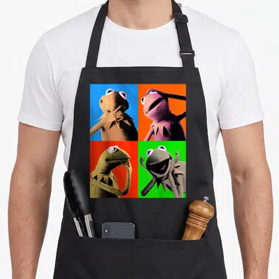 Pop frog aprons - Kermit the Frog in four colored squares with different poses — shown on a black cotton canvas apron against a white background