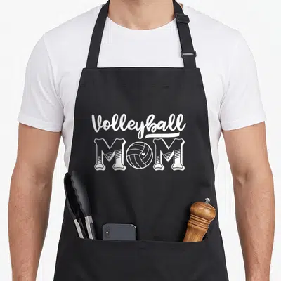 Vintage volleyball apron - White MOM text with volleyball graphic replacing the O letter — shown on a black cotton canvas apron against a white background