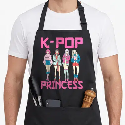 Funny pop princess apron - Four cartoon K-pop girls in pink and blue between K-POP and PRINCESS text — shown on a black cotton canvas apron against a white background