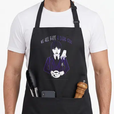 Dark ash wednesday apron - Girl with braids holding coffee and severed hand on shoulder under arched text WE ALL HAVE — shown on a black cotton canvas apron against a white background