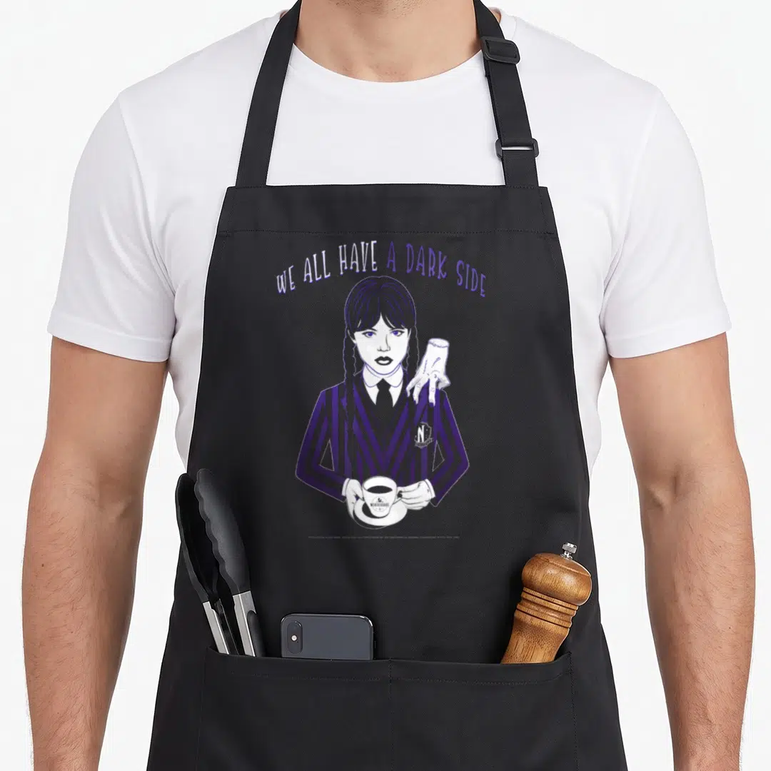 Dark ash wednesday apron - Girl with braids holding coffee and severed hand on shoulder under arched text WE ALL HAVE — shown on a black cotton canvas apron against a white background