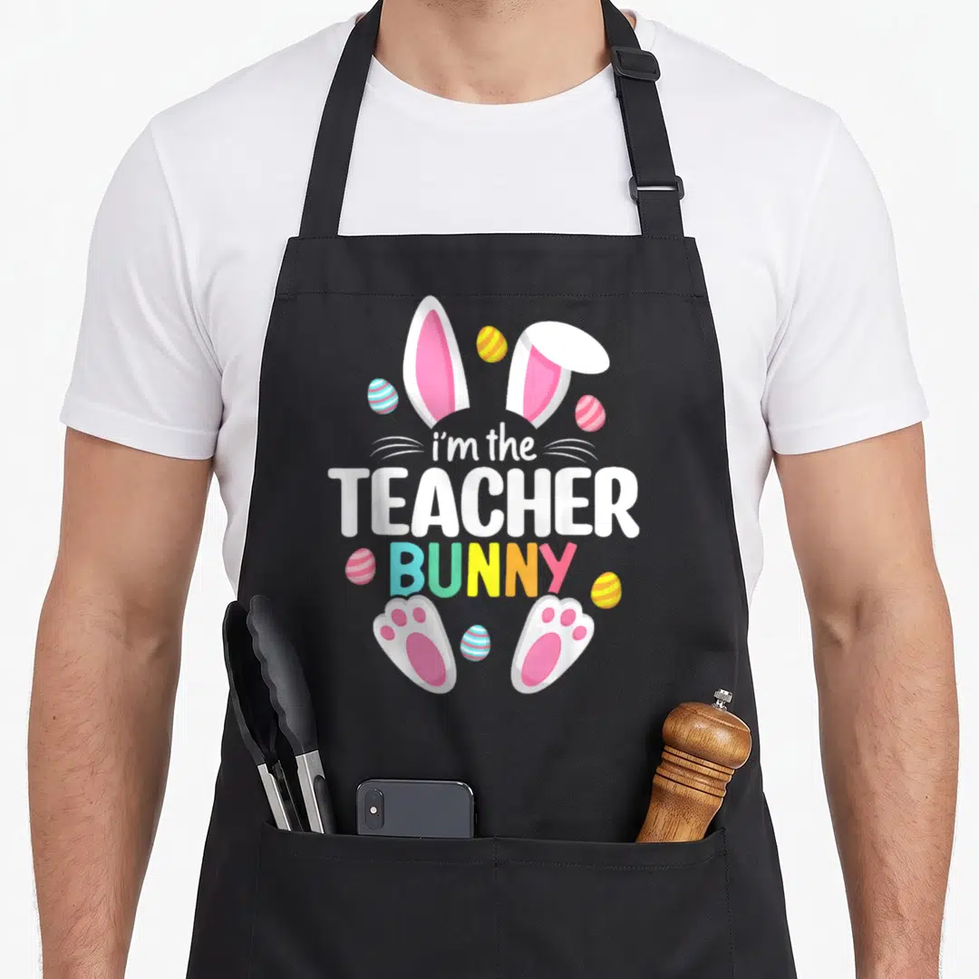 Teacher easter bunny aprons - Stacked i'm the TEACHER BUNNY text with pink ears, paws, and striped eggs in white pink — shown on a black cotton canvas apron against a white background