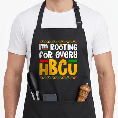 Rooting historical aprons - I'M ROOTING FOR EVERY HBCU text in white yellow red green with triangle borders on black bib — shown on a black cotton canvas apron against a white background