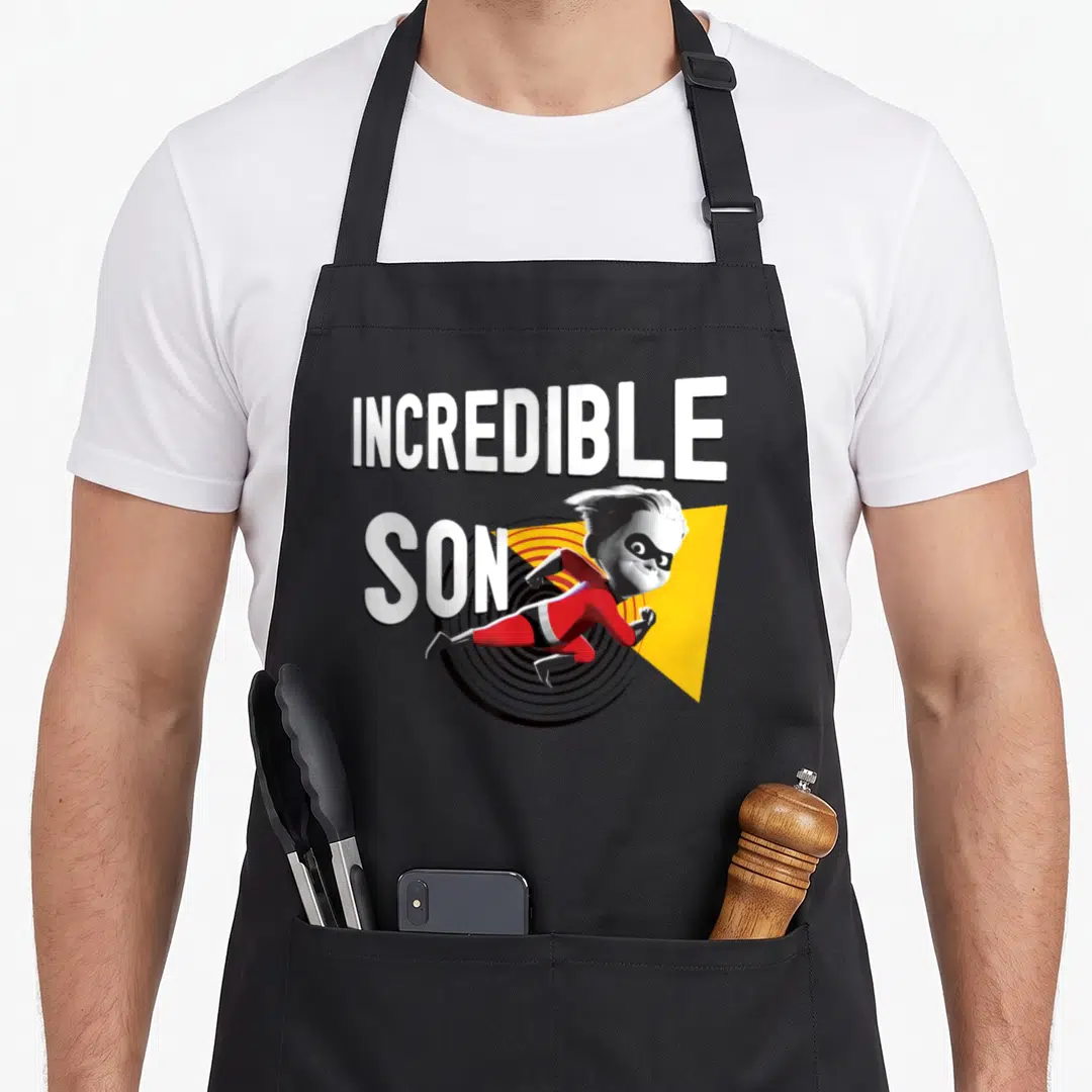 Funny incredible dad and son aprons - Running cartoon boy in red suit with INCREDIBLE SON text over yellow triangle — shown on a black cotton canvas apron against a white background