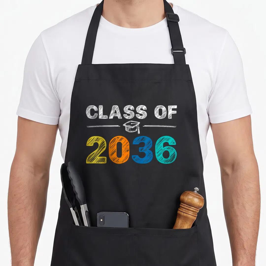 Graduation class first apron - CLASS OF 2036 text with multicolored numbers and a centered graduation cap illustration — shown on a black cotton canvas apron against a white background