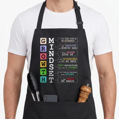 Growth classroom aprons - Vertical GROWTH MINDSET text with colored squares and motivational phrases on grey background — shown on a black cotton canvas apron against a white background