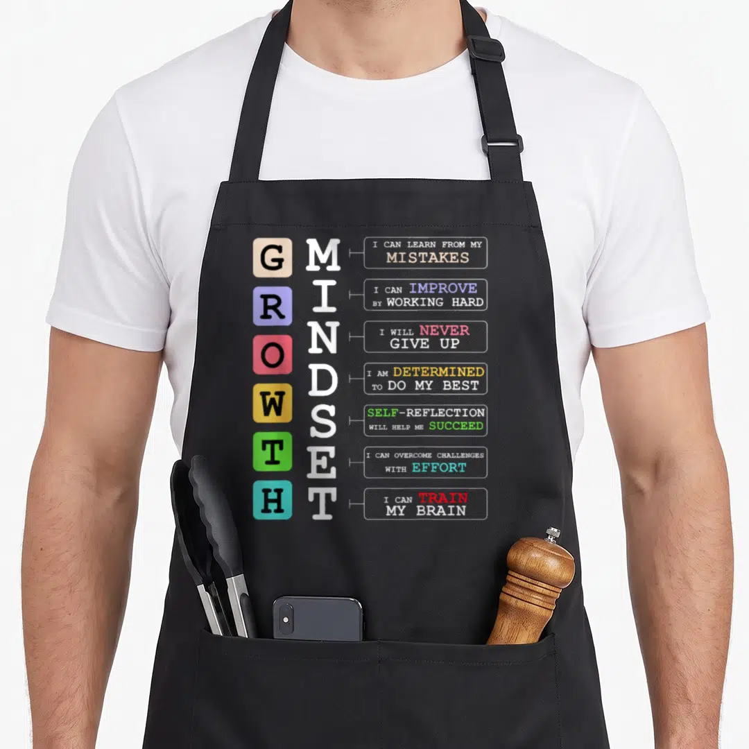 Growth classroom aprons - Vertical GROWTH MINDSET text with colored squares and motivational phrases on grey background — shown on a black cotton canvas apron against a white background