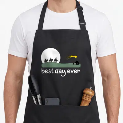 Nativity scene christmas apron - Three wise men on camels under white moon with best day ever text — shown on a black cotton canvas apron against a white background