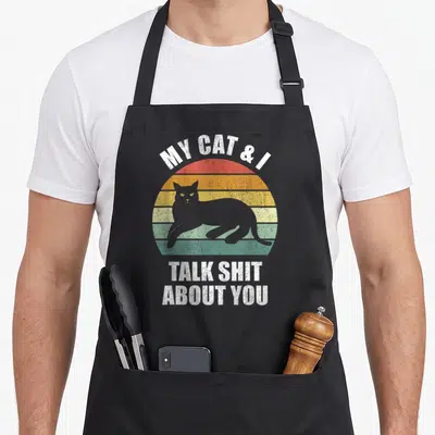 Funny talk cat apron - Retro sunset with grey cat silhouette and sarcastic white text — shown on a black cotton canvas apron against a white background