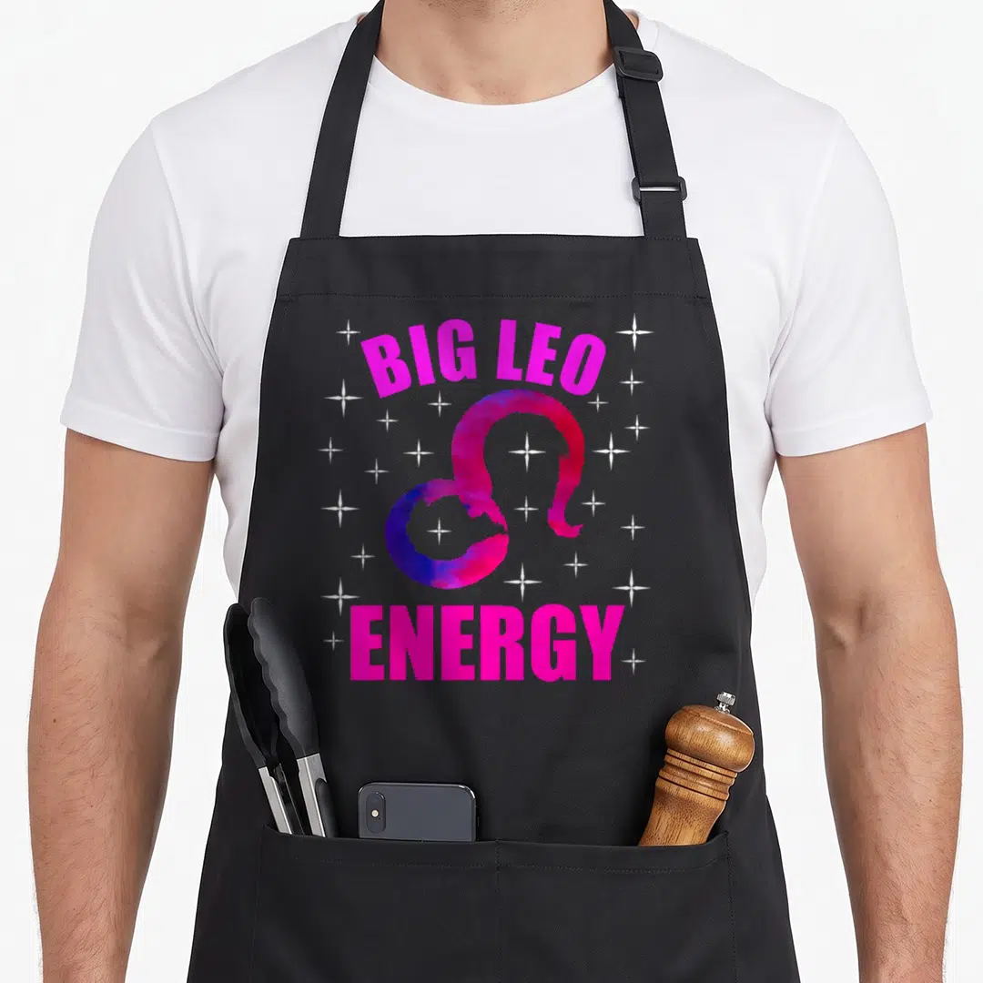 Energy zodiac birthday apron - Big Leo Energy text with purple Leo symbol and white stars — shown on a black cotton canvas apron against a white background