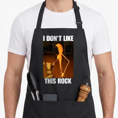 Marcus worm apron - Orange creature pointing at rocks with text I don't like this rock — shown on a black cotton canvas apron against a white background