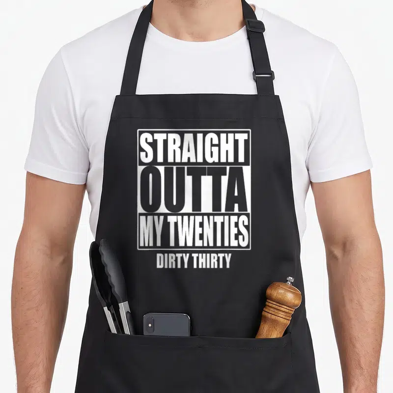 Twenty funny dirty aprons - White stacked text reading Straight Outta My Twenties Dirty Thirty inside a rectangular — shown on a black cotton canvas apron against a white background