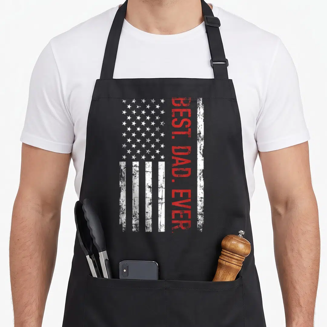 Flag father day apron - Distressed USA flag with vertical red BEST. DAD. EVER text on white background — shown on a black cotton canvas apron against a white background