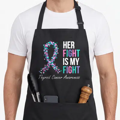 Thyroid cancer family aprons - Heart-shaped awareness ribbon in pink purple teal and white next to stacked bold text — shown on a black cotton canvas apron against a white background