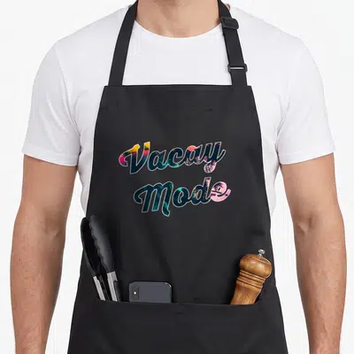 Sunrise summer aprons - Stacked Vacay Mode text filled with tropical palm trees and sunset gradient colors — shown on a black cotton canvas apron against a white background