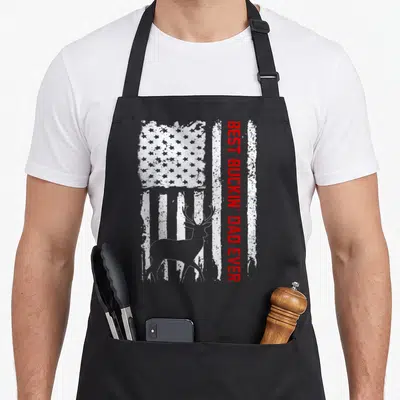 Flag buckin father day apron - Distressed USA flag background with grey deer silhouette and vertical red text — shown on a black cotton canvas apron against a white background