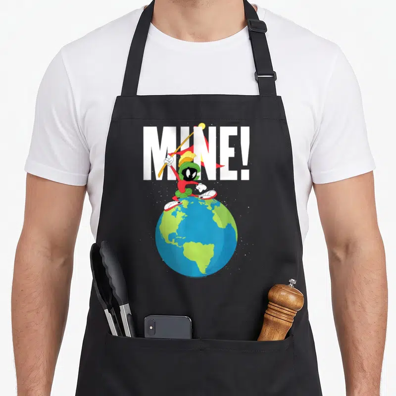 Marvin tunes apron - Cartoon character on globe holding spear with MINE! text in white and colored details — shown on a black cotton canvas apron against a white background