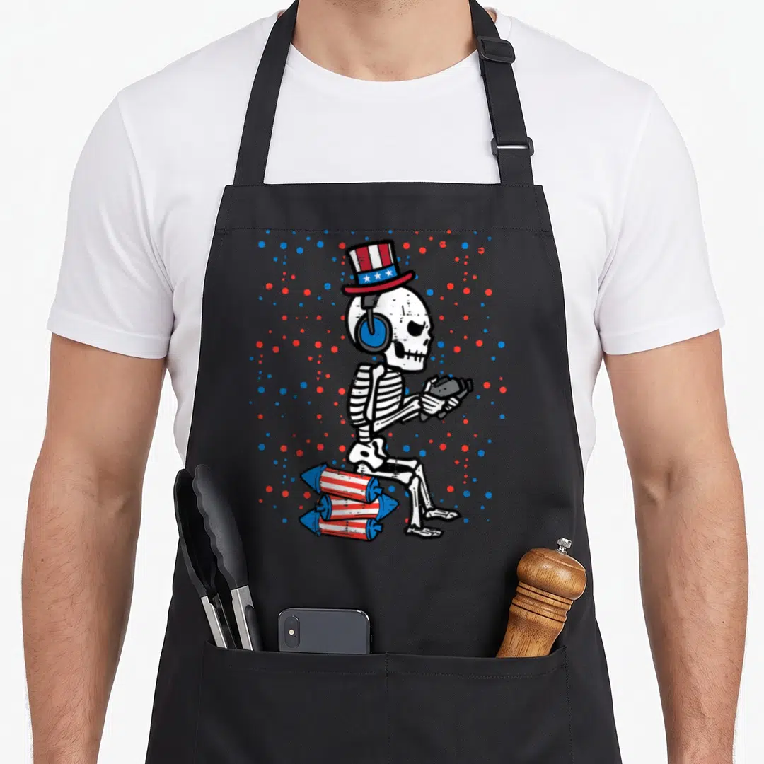 Skeleton 4th of july apron - Cartoon skeleton in patriotic top hat and headphones sitting on rockets surrounded by red — shown on a black cotton canvas apron against a white background