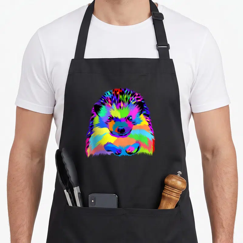 Pop hedgehog animal apron - Multicolored cartoon hedgehog in blue, green, yellow, red, and purple pop art style — shown on a black cotton canvas apron against a white background