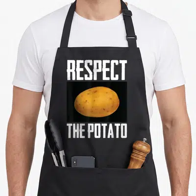Respect vegetable apron - Photo of yellow potato in black box with white Respect The Potato text — shown on a black cotton canvas apron against a white background
