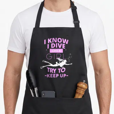 Scuba i love snorkeling apron - Pink text I know I dive like a girl try to keep up with white diver silhouette — shown on a black cotton canvas apron against a white background