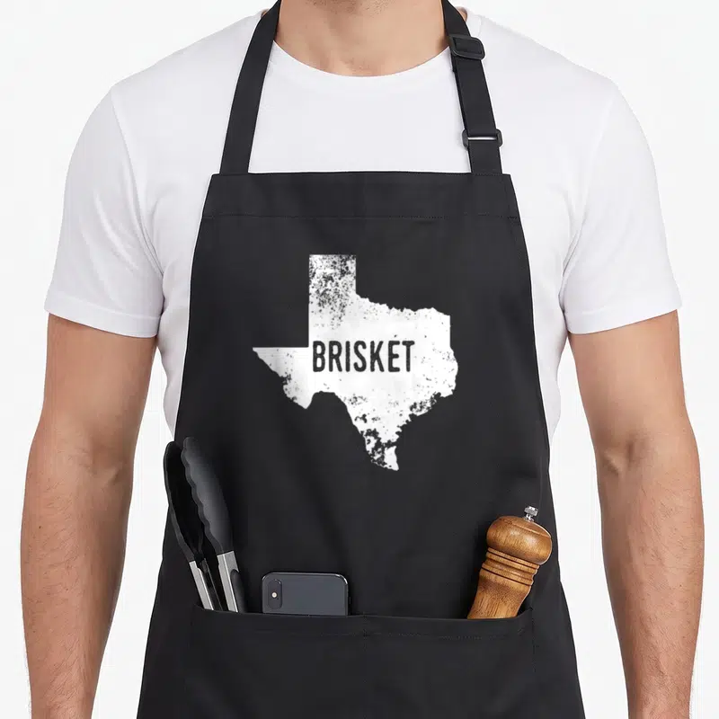 State brisket texas apron - White distressed Texas state silhouette with grey BRISKET text across center — shown on a black cotton canvas apron against a white background