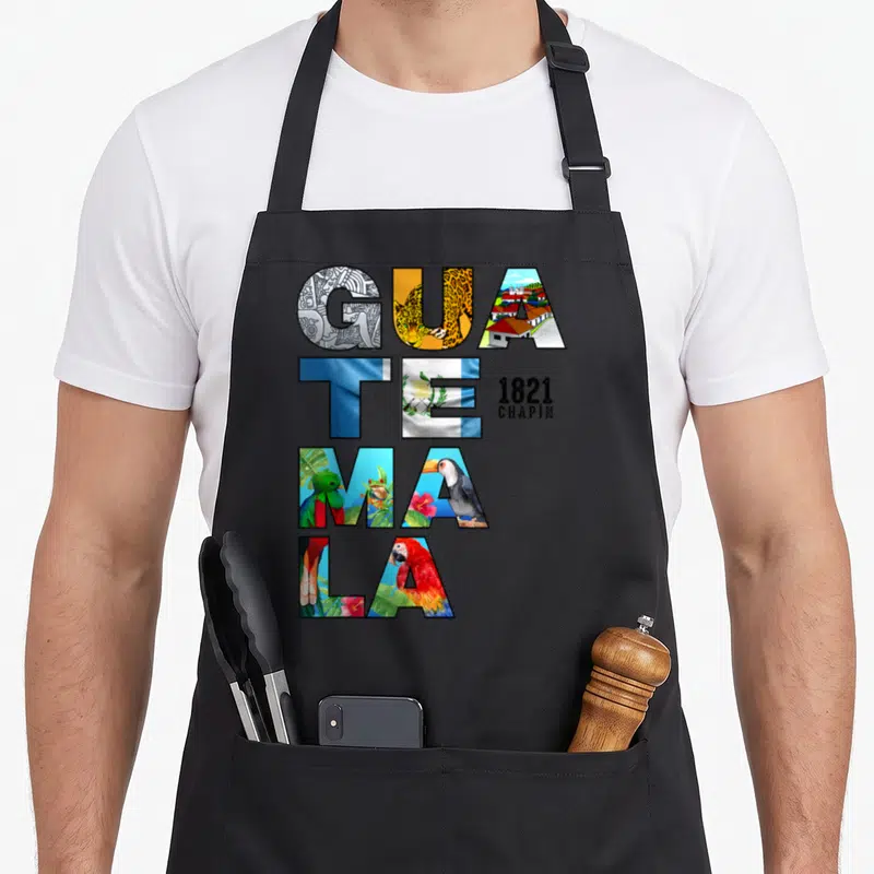 Funny chapin guatemala apron - Stacked GUATEMALA letters filled with quetzal, jaguar, flag, and 1821 CHAPIN text — shown on a black cotton canvas apron against a white background