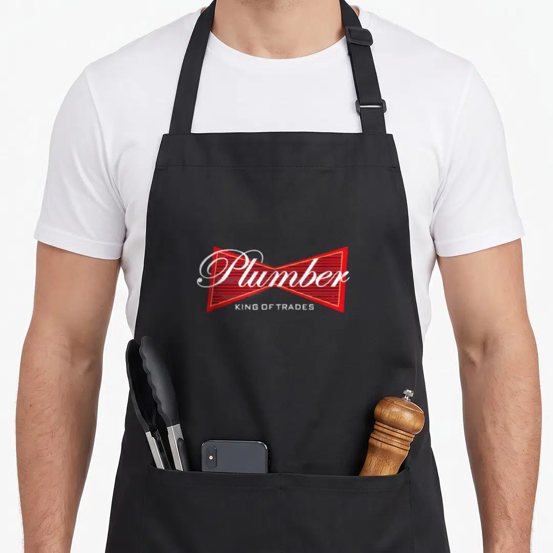 Plumber king apron - Red striped bowtie graphic with white Plumber script and KING OF TRADES text — shown on a black cotton canvas apron against a white background