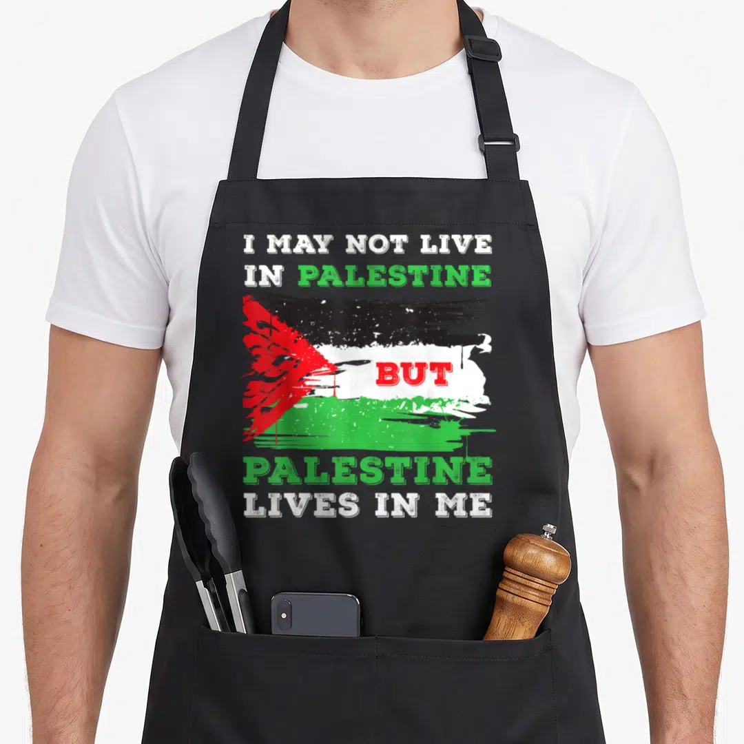 Flag live palestinian apron - Distressed Palestinian flag with text I MAY NOT LIVE IN PALESTINE BUT PALESTINE LIVES — shown on a black cotton canvas apron against a white background