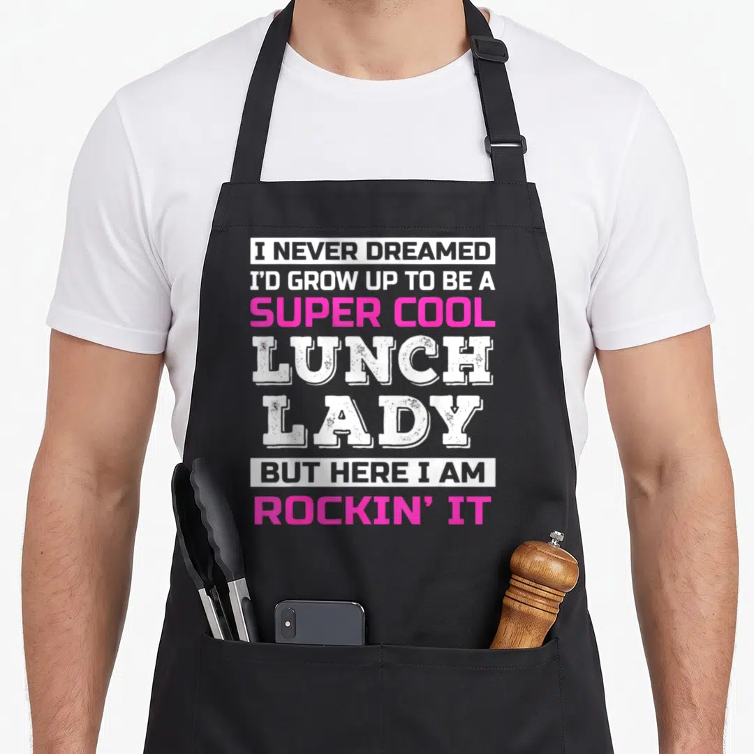 Funny appreciation lunch lady apron - Stacked white and pink text reading super cool lunch lady rockin it — shown on a black cotton canvas apron against a white background