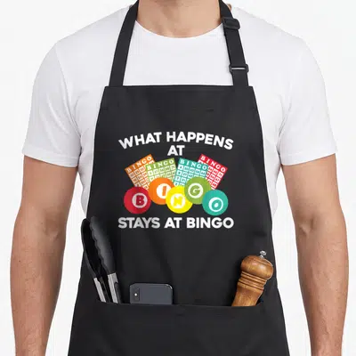 Gambling bingo aprons - White text surrounding five colorful bingo balls and four fanned bingo cards — shown on a black cotton canvas apron against a white background