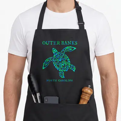 Outer travel aprons - Distressed blue and green sea turtle with Outer Banks North Carolina text — shown on a black cotton canvas apron against a white background