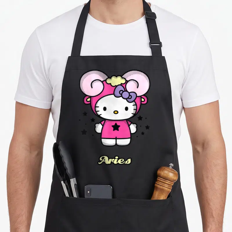 Zodiac aries kitchen apron - Hello Kitty in pink ram costume with purple bow and black stars surrounding yellow Aries — shown on a black cotton canvas apron against a white background
