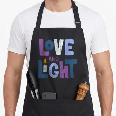 Funny light hanukkah apron - LOVE AND LIGHT text with candle I in purple blue white and yellow — shown on a black cotton canvas apron against a white background