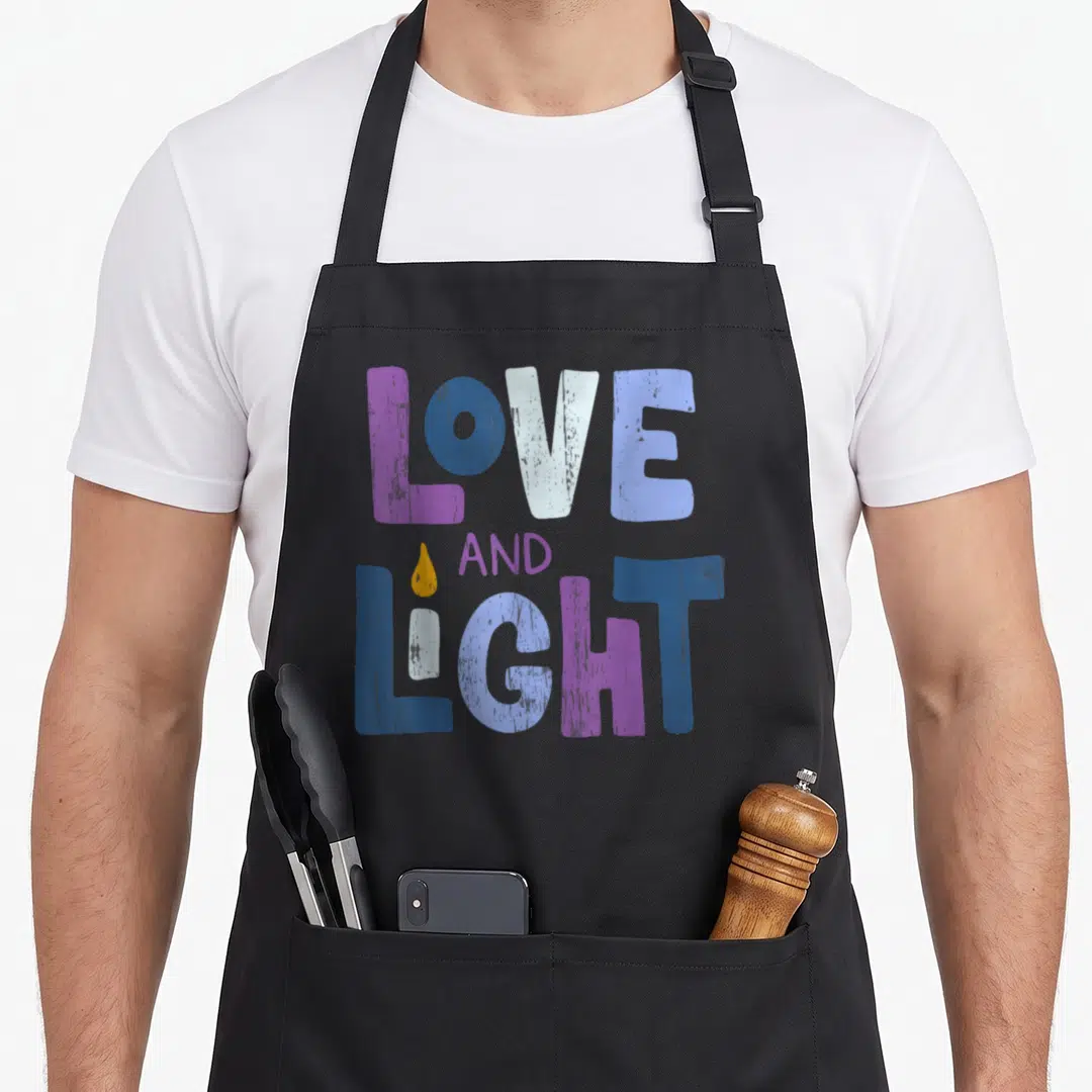 Funny light hanukkah apron - LOVE AND LIGHT text with candle I in purple blue white and yellow — shown on a black cotton canvas apron against a white background