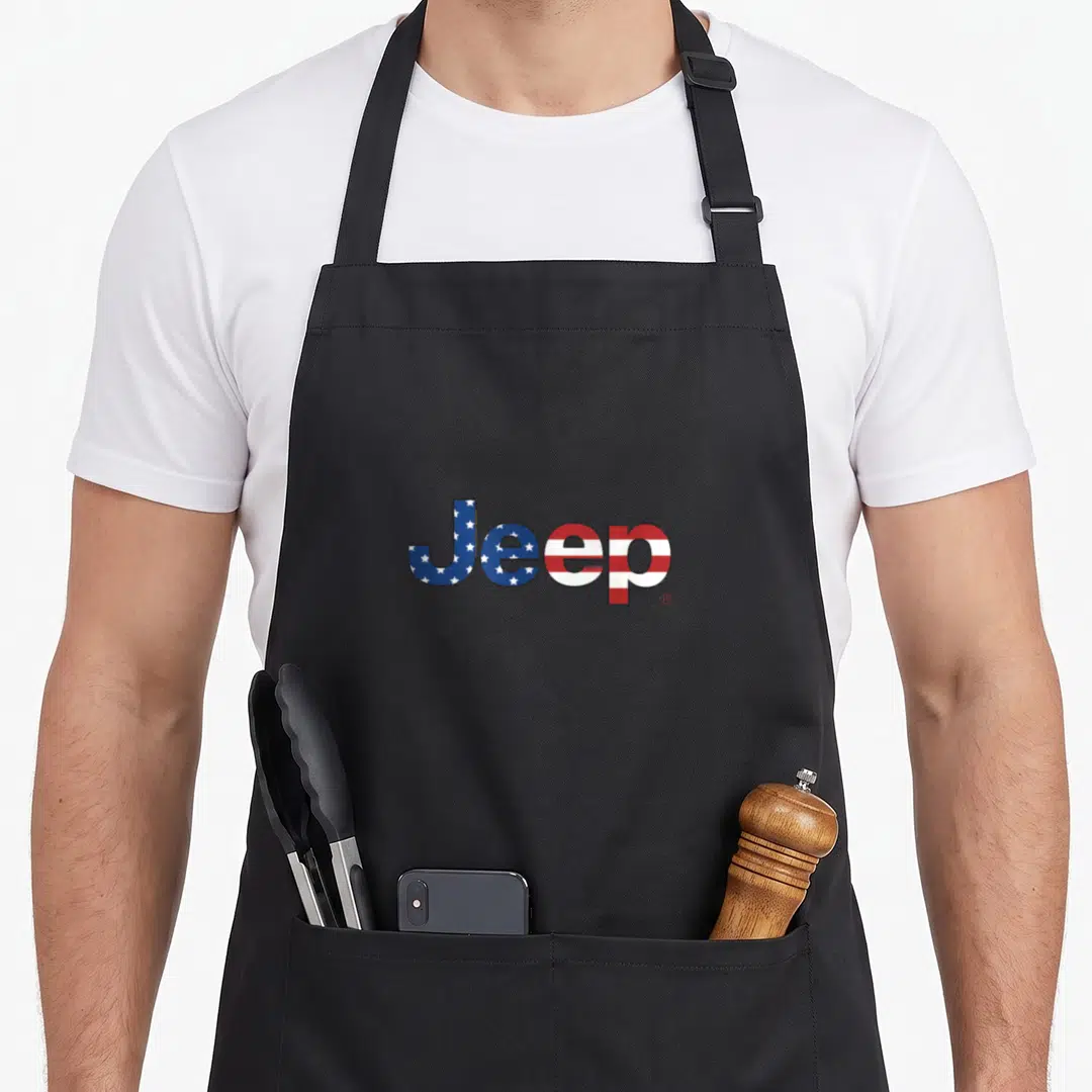 Jeep american flag apron - Jeep text filled with blue stars and red white stripes pattern — shown on a black cotton canvas apron against a white background