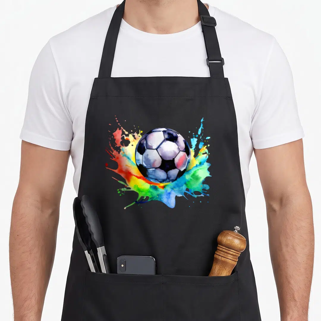 Watercolor football team aprons - Soccer ball centered on blue red yellow green white watercolor paint splashes — shown on a black cotton canvas apron against a white background