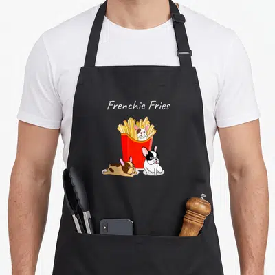 Frenchie fry french bulldog apron - Cartoon Frenchie Fries text with red fry box and three french bulldogs in white — shown on a black cotton canvas apron against a white background