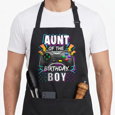 Funny aunt video game apron - Cartoon game controller with lightning bolts and text Aunt of the Birthday Boy in white — shown on a black cotton canvas apron against a white background