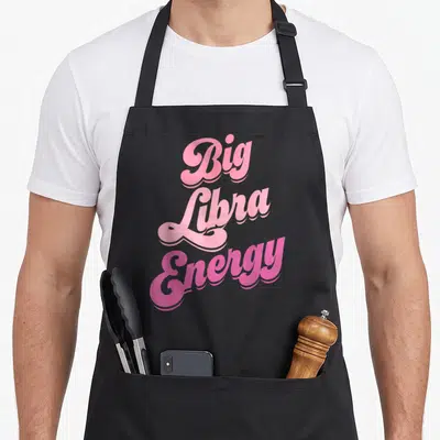 Libra energy zodiac aprons - Pink retro cursive text reading Big Libra Energy stacked vertically — shown on a black cotton canvas apron against a white background
