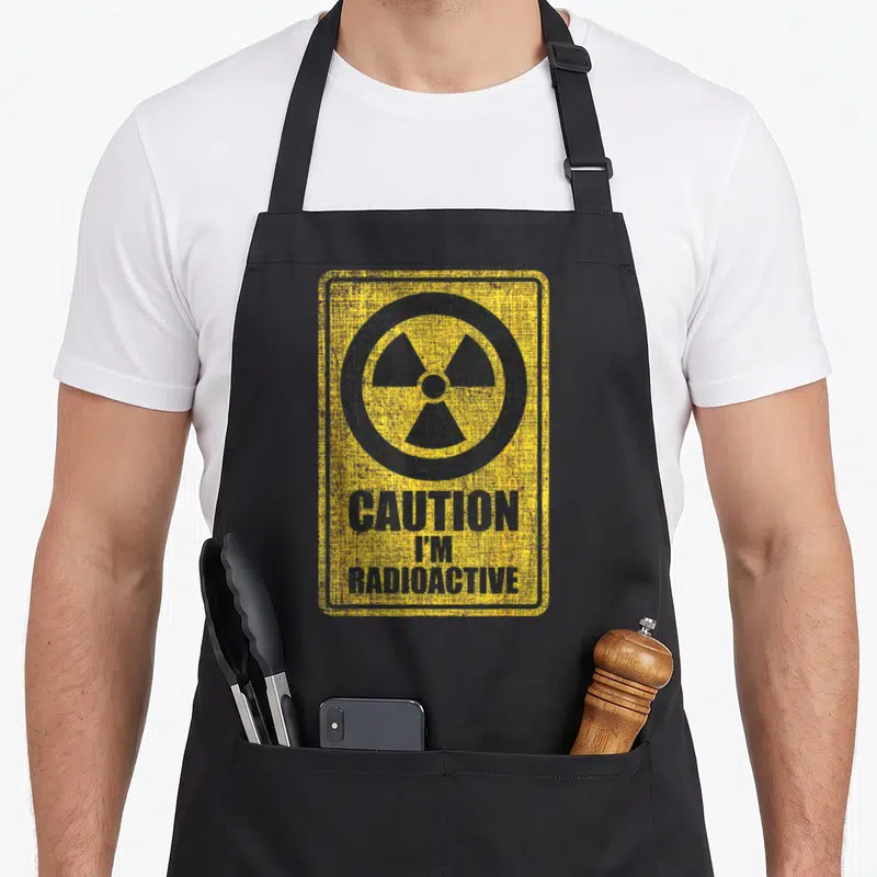 Caution radiation aprons - Yellow sign with black radiation symbol and text CAUTION I'M RADIOACTIVE — shown on a black cotton canvas apron against a white background