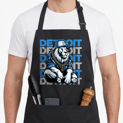 Youth lion apron - Cartoon lion in cap and gold chain before five stacked Detroit text lines in blue and grey — shown on a black cotton canvas apron against a white background