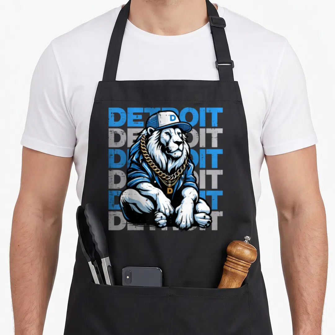 Youth lion apron - Cartoon lion in cap and gold chain before five stacked Detroit text lines in blue and grey — shown on a black cotton canvas apron against a white background