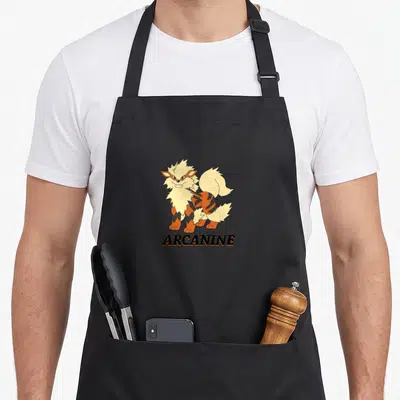 Funny arcanine trend apron - Cartoon orange and cream dog standing above black ARCANINE text — shown on a black cotton canvas apron against a white background