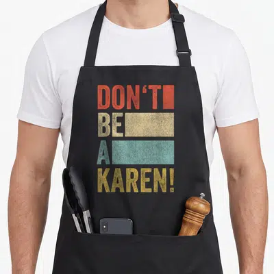 Meme gag aprons - Stacked red beige blue and yellow text reading DON'T BE A KAREN — shown on a black cotton canvas apron against a white background