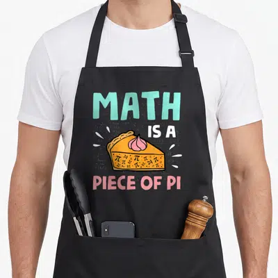 Math pie apron - Cartoon pie slice filled with pi symbols and text Math Is A Piece Of Pi on grey background — shown on a black cotton canvas apron against a white background