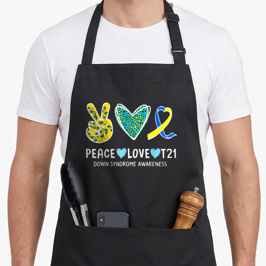 Cure ribbon apron - Peace hand, leopard heart, and ribbon with PEACE LOVE T21 text in yellow blue and white — shown on a black cotton canvas apron against a white background