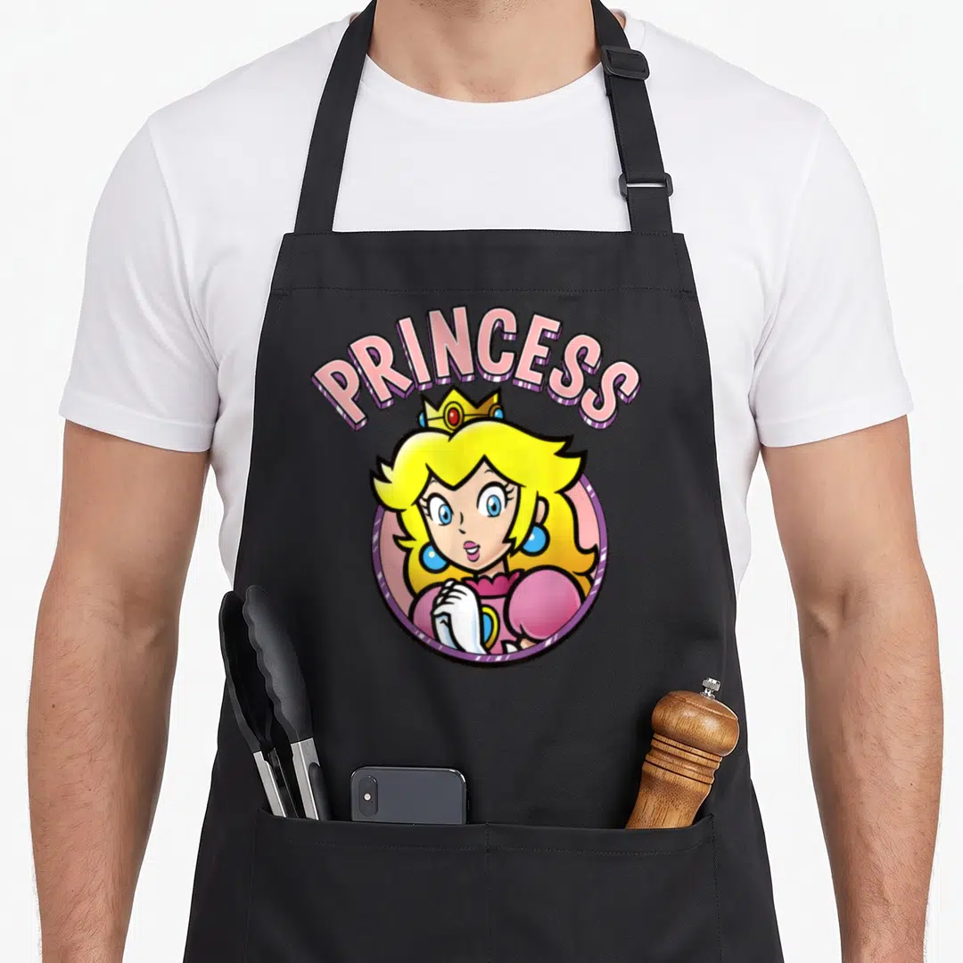 Peach portrait princess apron - Princess Peach cartoon portrait with arched PRINCESS text in pink and yellow — shown on a black cotton canvas apron against a white background
